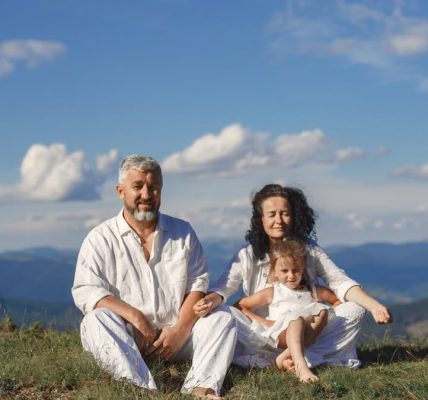 A happy family enjoys a sunny day outdoors, sitting together on a grass field.