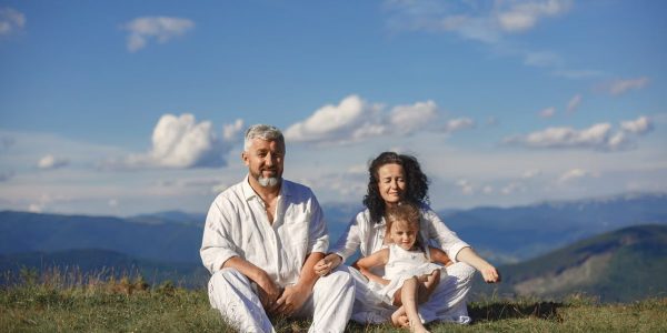 A happy family enjoys a sunny day outdoors, sitting together on a grass field.
